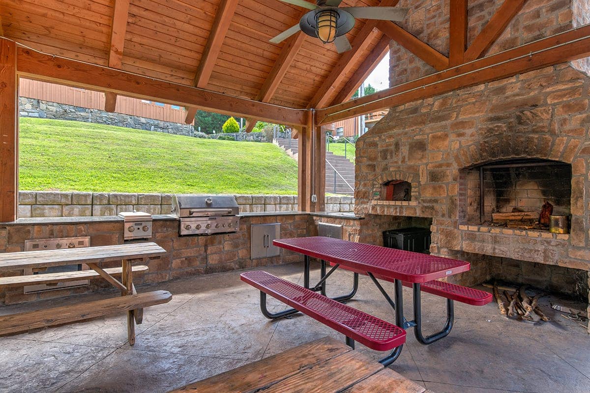 an outdoor covered patio with a large grill and fireplace near picnic tables