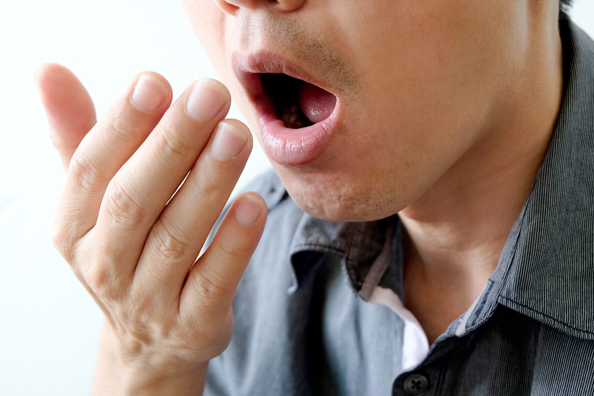 man blowing into his hand showing that Alcohol Brings Bad Breath