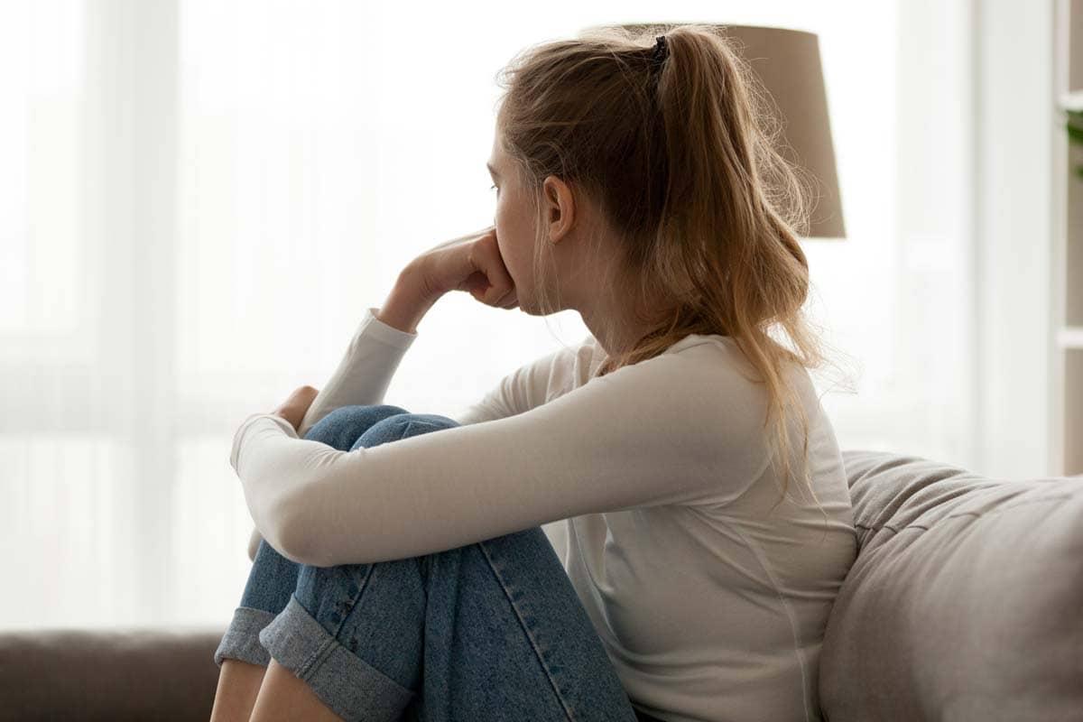 a young woman sits on a couch and considers the effects of an eating disorder