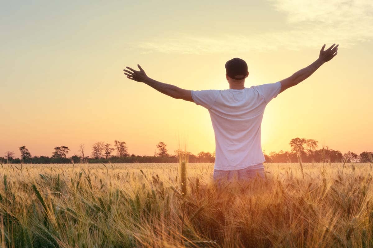 a man stretches out his arms towards the sunrise as he experiences sober living