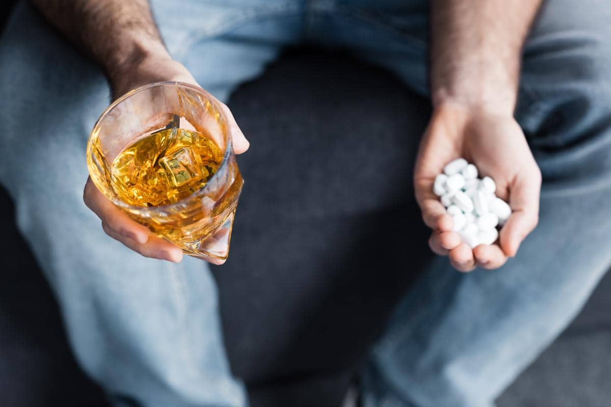 man holding alcohol and a handful of pills