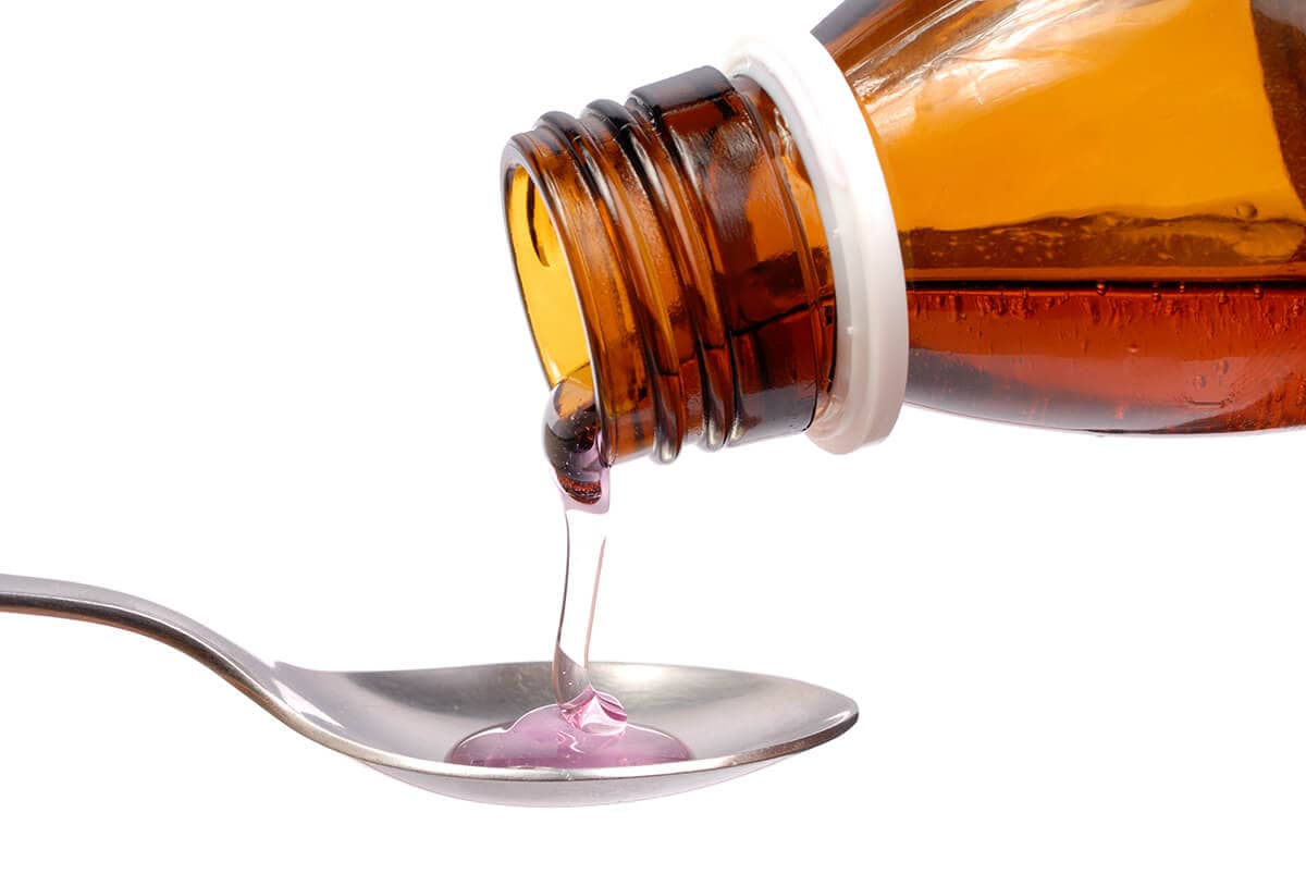 a person pouring cough syrup on a spoon to participate in cough syrup abuse