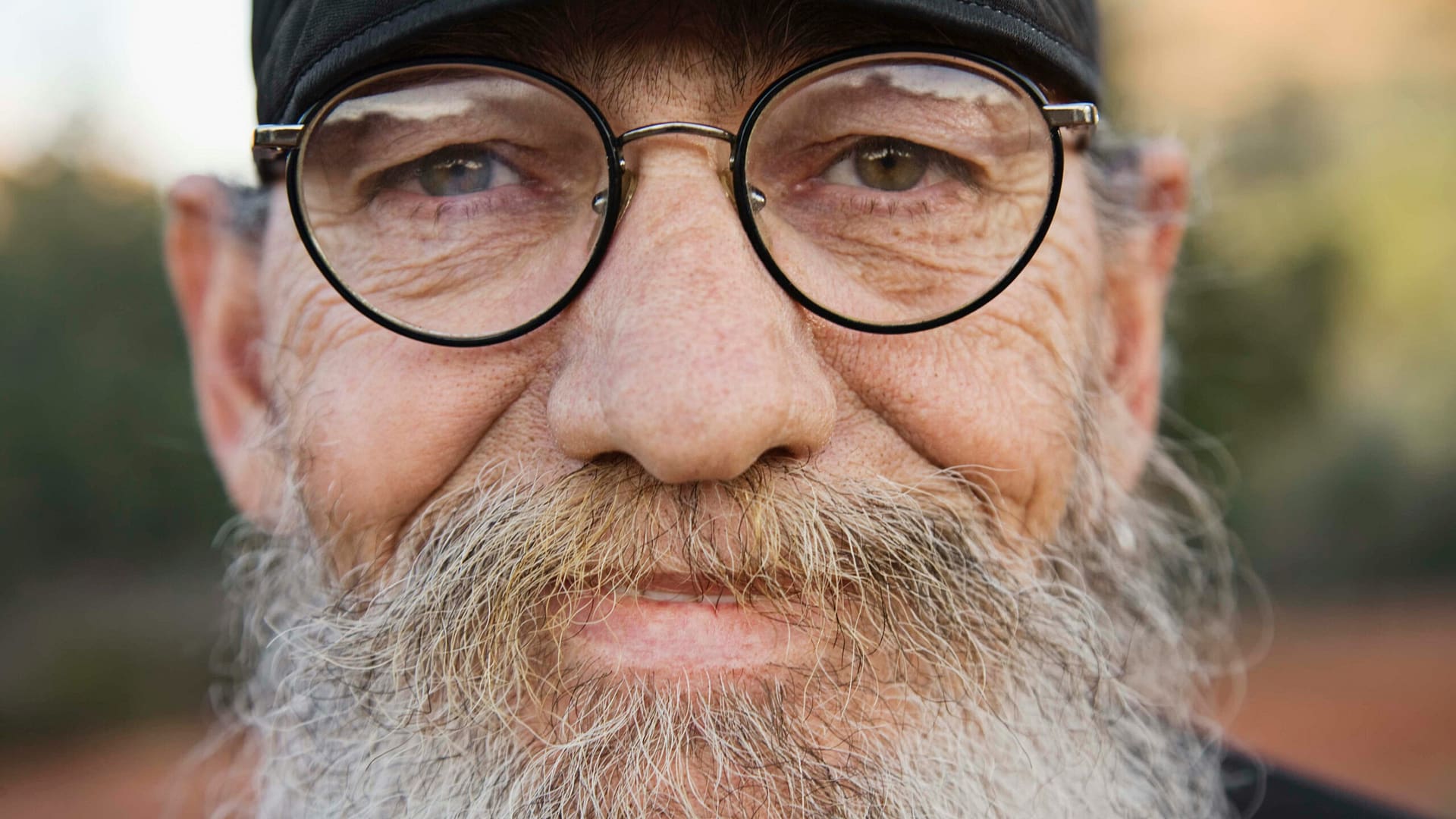 Close-up of an older man with glasses and a beard, looking calm and thoughtful