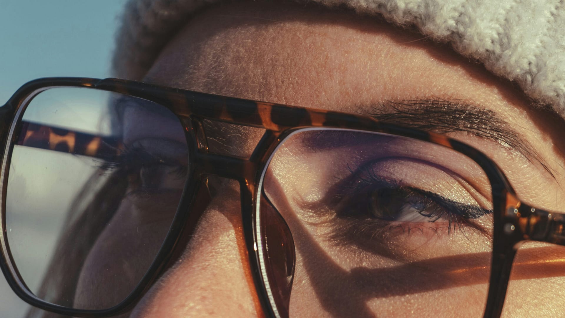 Close-up of a person wearing tortoiseshell glasses and a knit hat in sunlight