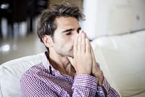 Man sitting on sofa with hands to face, dealing with an opiate withdrawal.