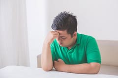 Man in green shirt at table with knows he needs an alcohol addiction treatment center.