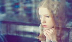 Sad young woman at window worried about her last opioid overdose.