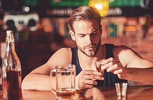 A man struggling with addiction contemplates his next drink at the bar.