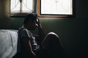 a young man in the cycle of addiction sits depressed at the end of a bed