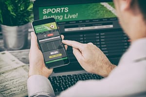 a person with sports betting addiction places wagers on a phone and computer