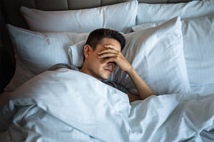 a man lays in bed in pain after self-medicating with alcohol