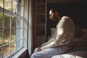 a man sits on his bed as he considers the signs of alcohol withdrawal