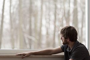 Bearded man looking out window at a forest contemplating how his fentanyl abuse happened.