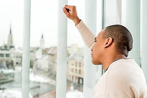 Depressed man looking out window suffering with Pain Pill Withdrawal symptoms
