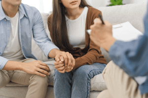 Man holds hands with family member on couch as they endure family therapy program