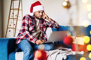 man in santa hat on laptop deals with holiday loneliness and isolation