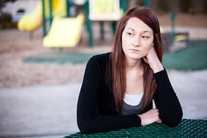 Woman at a table at playground thinking she needs a rehabilitation center.