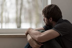 Bearded man looking out window confused about CBT meaning during rehab.