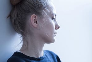 Sad woman against gray wall going through crack addiction recovery.