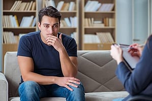 Man on couch considering info about drug addiction rehabilitation from counselor.