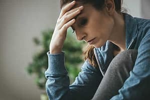 Woman with hand to forehead worried about genetics and addiction