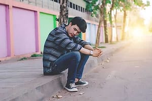 Young man on curb may need relapse prevention strategies for his drug addiction recovery