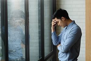 Man at window with hand to head may need an ativan addiction rehab program