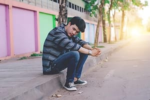 Sad young man on curb tired of self medicating depression