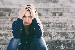 Depressed young woman on steps hold head experiencing some types of mood disorders