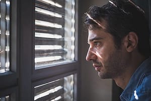 Man staring through blinds suffering painkiller addiction symptoms