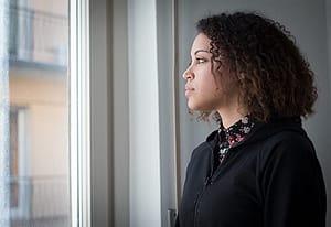 Sad young woman looking out window thinking that Adhd awareness month may get her to addiction help