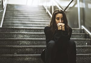 Sad young woman on dark steps suffering with depression from abuse of drugs