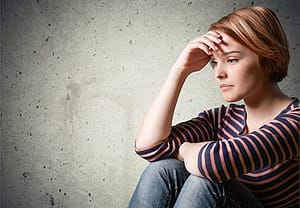 Young woman with hand to forehead contemplating using a sober living house after rehab