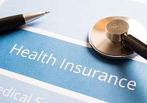 a stethoscope and pen lie on top of a paper that reads "health insurance" and covers accepted insurances
