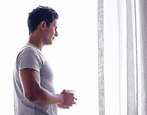 Young man looking out window pondering how long does it take to detox from alcohol