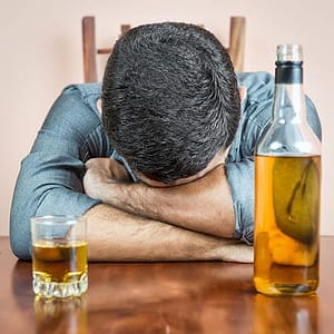 Man with head on table, drinks standing by, needs alcohol detox treatment.