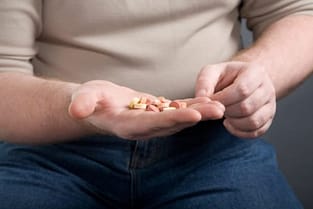 man looking at handful of pills thinking about attending the painkiller detox center