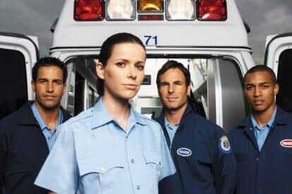 Four young paramedics standing at the rear of an ambulance