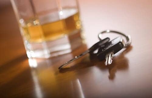 Car keys sitting next to a glass of alcohol