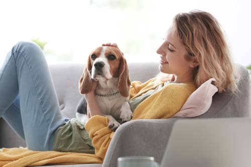 woman in yellow sweater sitting on couch petting dog as she considers going to addiction treatment programs