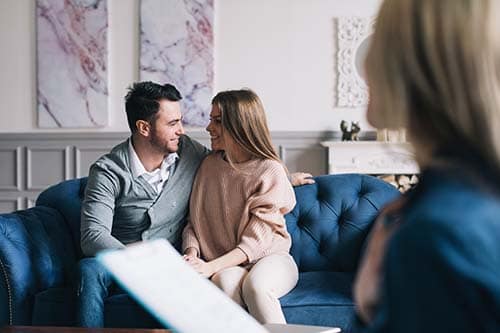 Couple snuggles on couch as their couples therapy therapist helps them get closer