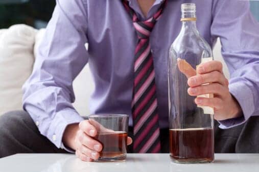 Businessman holding a bottle and cup full of alcohol