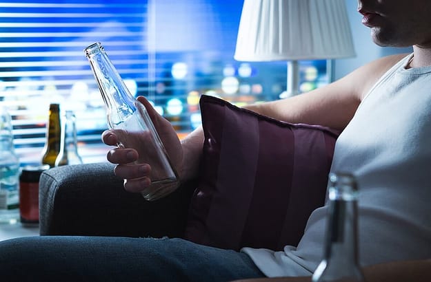 a person holds an empty beer bottle thinking about beating alcohol addiction