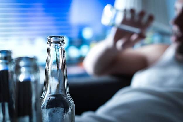 Man surrounded by empty beer bottles showing symptoms of alcohol poisoning