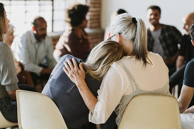 a woman hugging her daughter as they discuss examples of recovery group topics in a a group setting