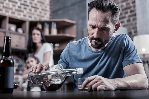 family shying away from man pouring another shot of whiskey showing the need for alcohol addiction treatment in florida