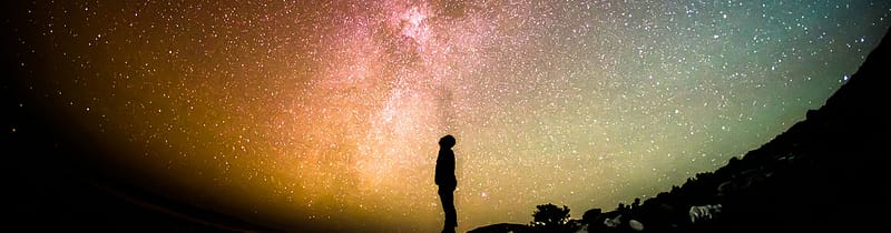 silhouette of a person looking at a colorful night sky