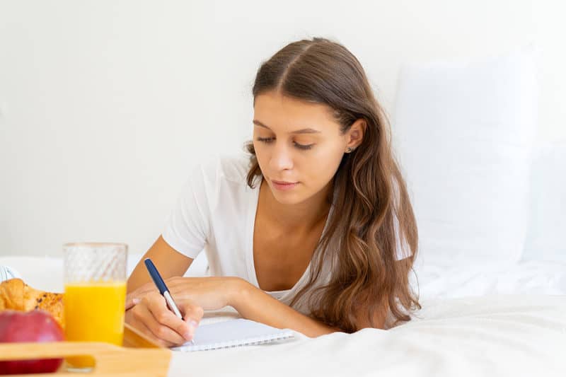 A woman tracking her addiction recovery by writing in a journal at home.