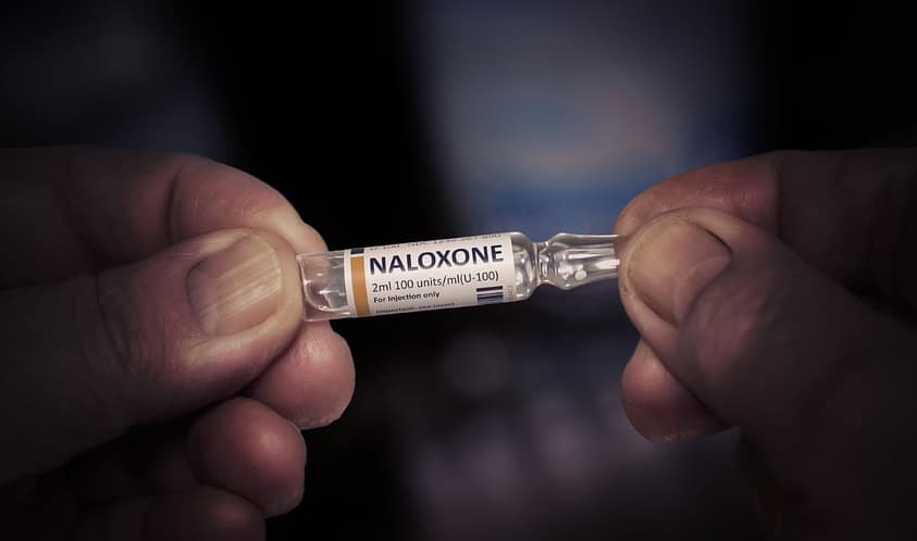 A close up of a man’s hands holding a naloxone injection.
