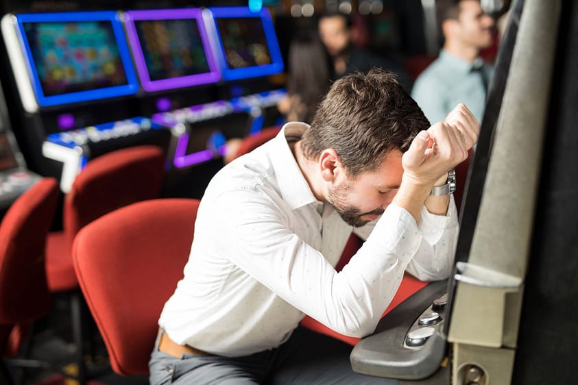 a young man looking despaired at a slot machines, one of the signs of a gambling addiction